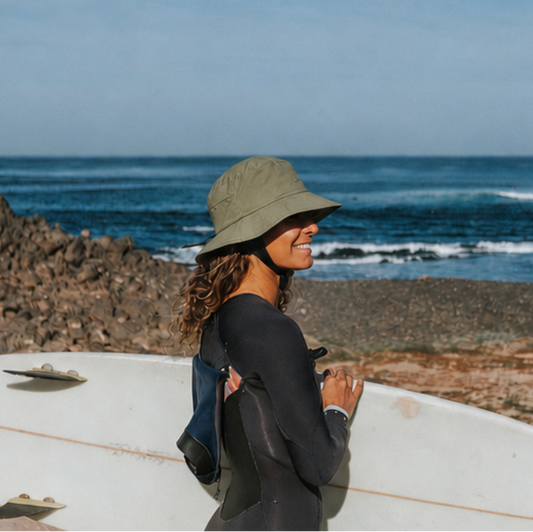 women wearing a surf hat helmet holding her surfboard about to go surf