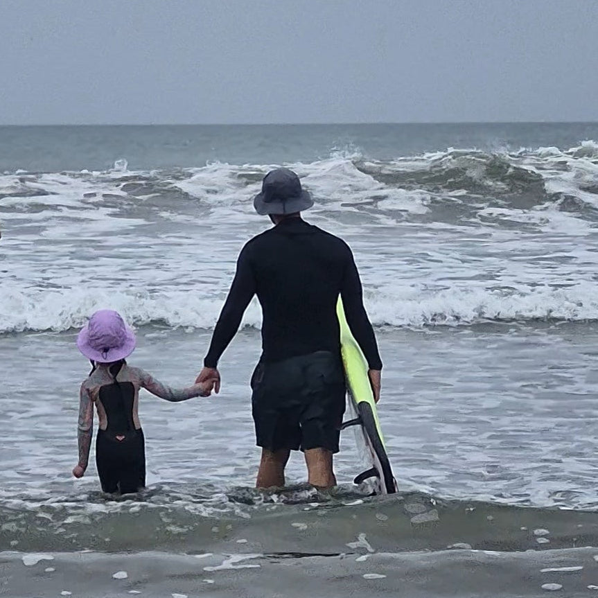 Dad and daughter going for a surf wearing surf hat helmets 