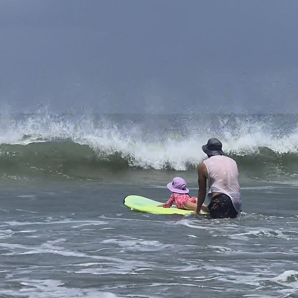 Girl learning how to surf wearung a surf hat helmet on a foamie surfboard 