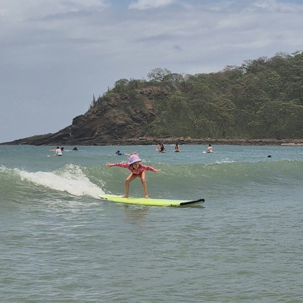 Little girl wearing a surf hat helmet on a wave learning how to surf 
