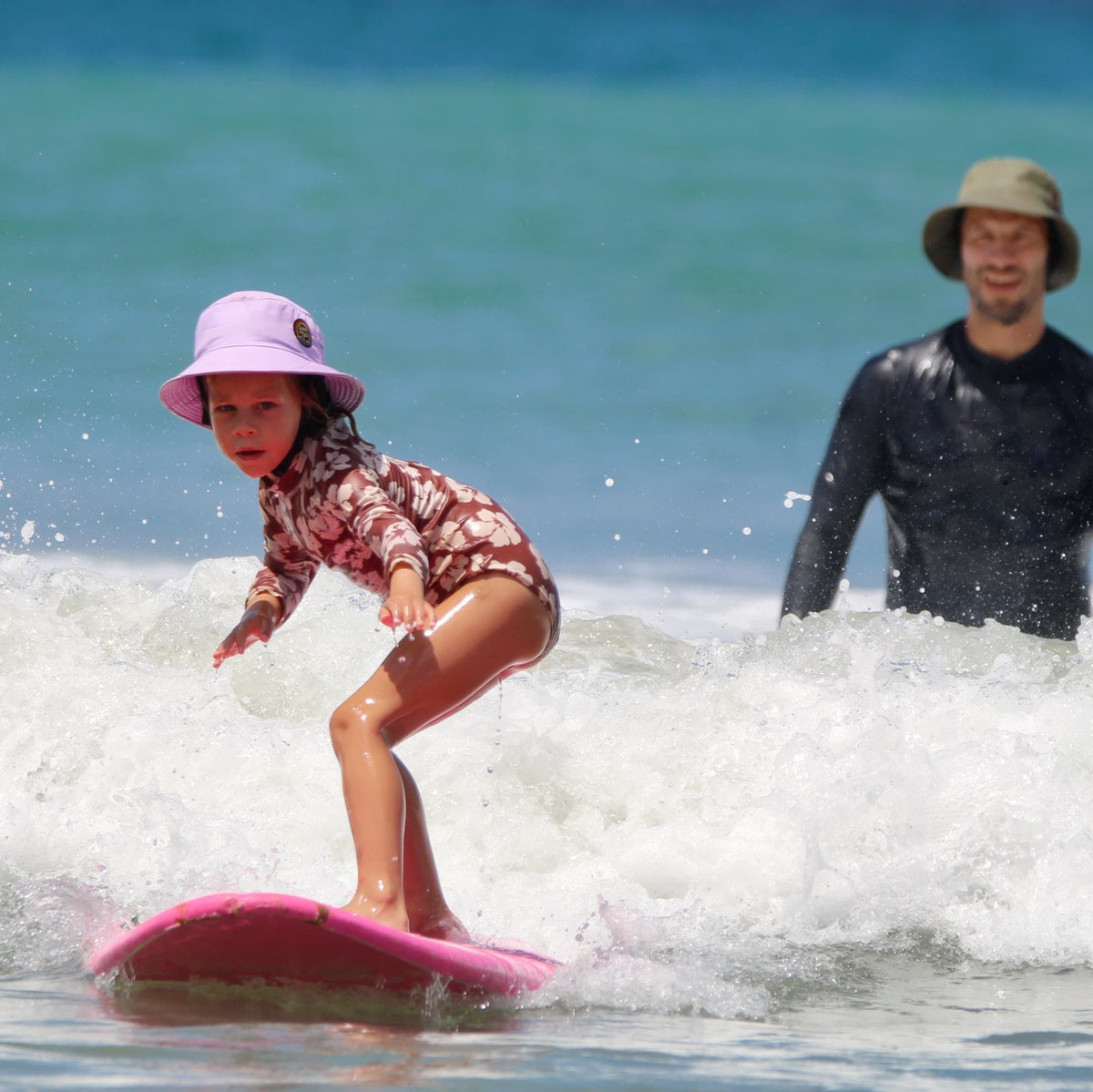 girl wearing surf hat helmet learning how to surf with her dad
