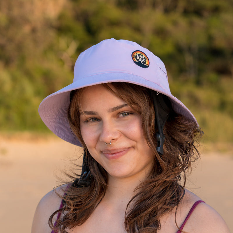 Woman wearing a surf hat helmet  lilac on a beach red hair