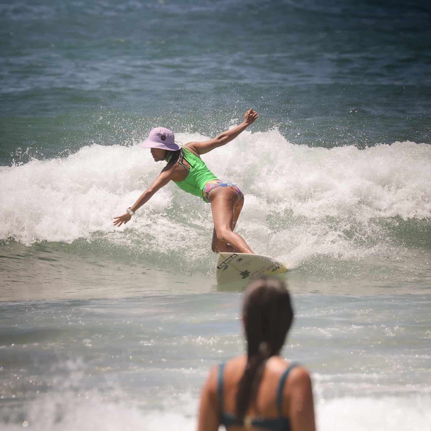 surfer wearing a lilac helmet bucket hat on a wave surfing a shotboard