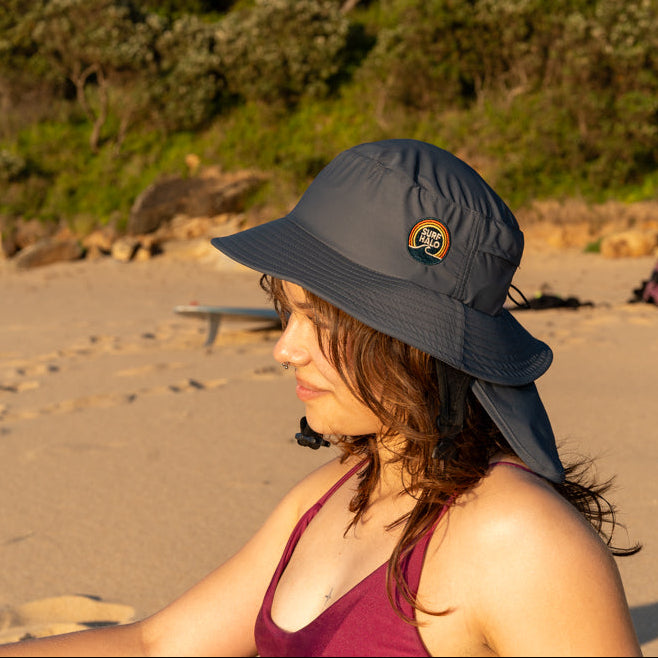 woman wearing surf hat helmet black on the beach with a removable neck flap adjustable