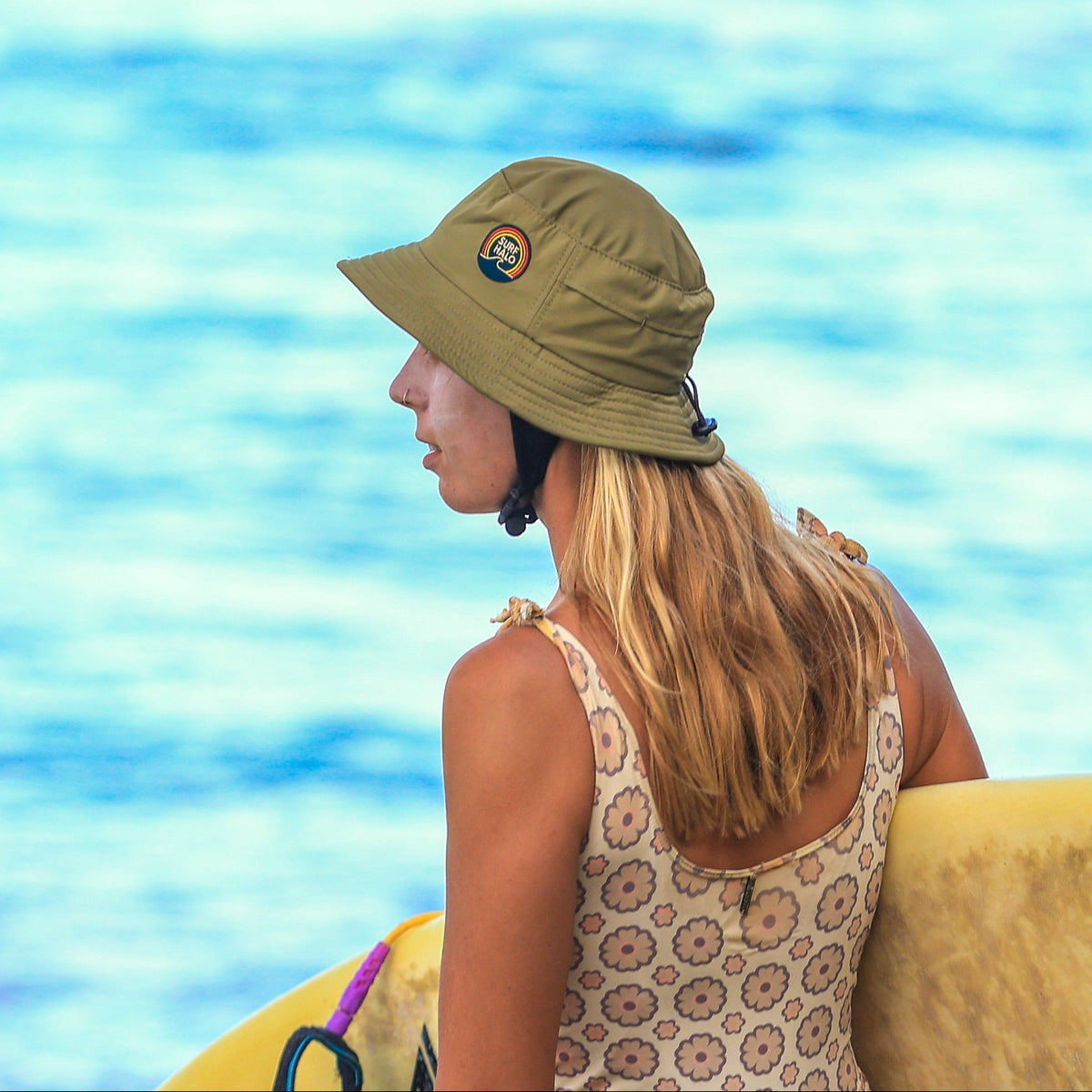 women wearing a surf bucket helmet hat holding a surfboard at the beach 