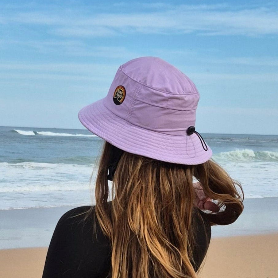 girl with a surf hat lilac holding a surfboard on the beach