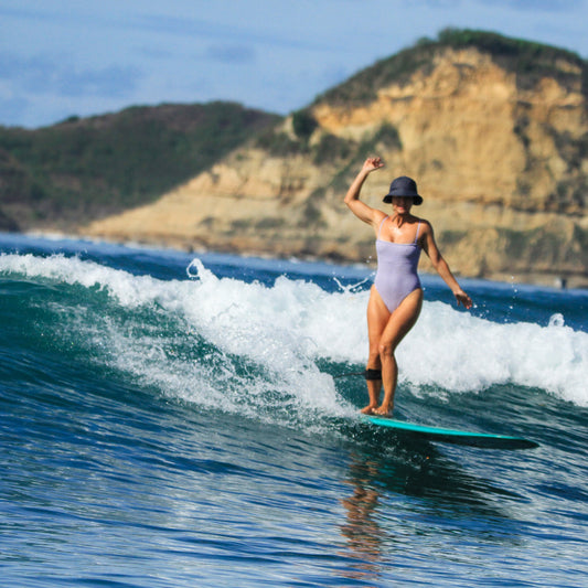 Woman surfing on a wave with a mountainous landscape in the background