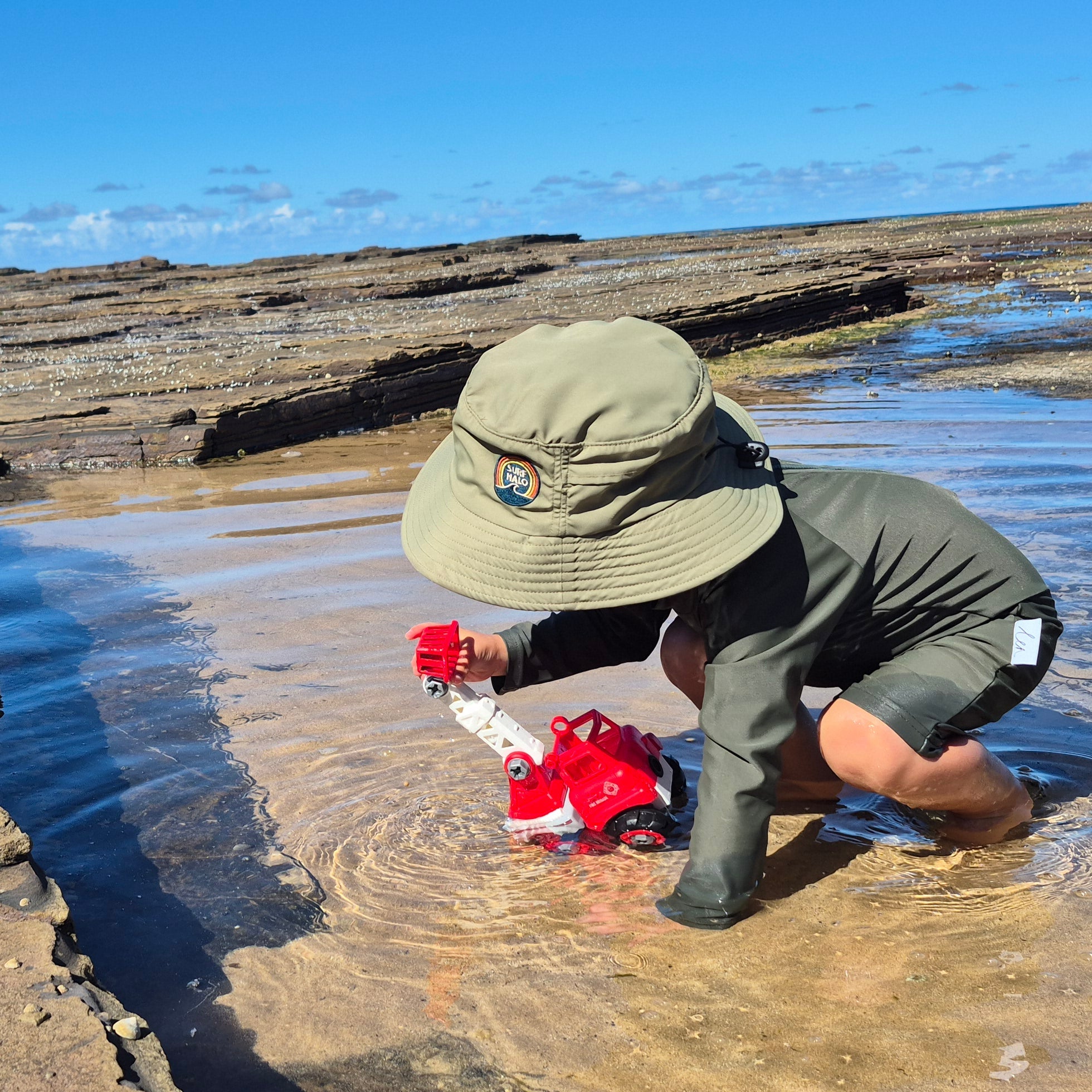 Toddler playing on reef pool wearing a surf hat green olive
