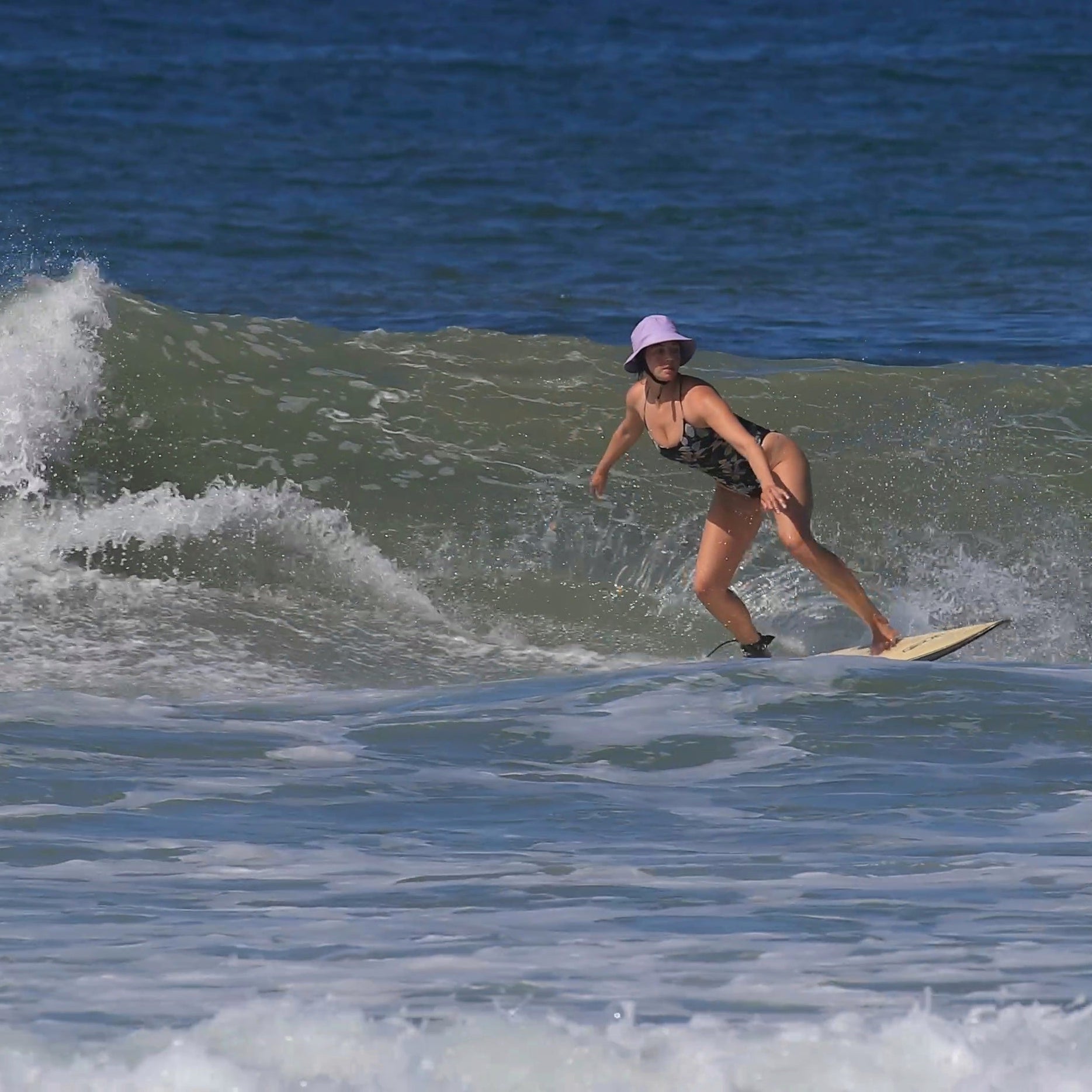 surfer girl on a wave wearing lilac surfing hat on a wave shortboard